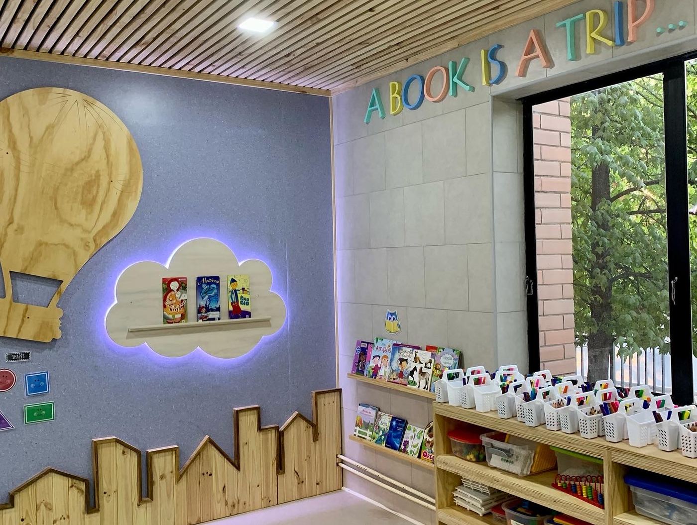 Rincón de lectura con nube iluminada y estantes bajo el ventanal