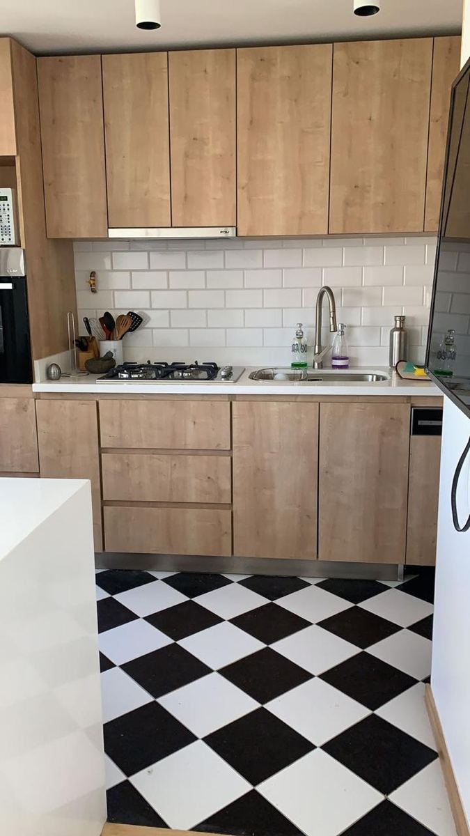Cocina con muebles de madera clara, azulejo blanco y piso damero